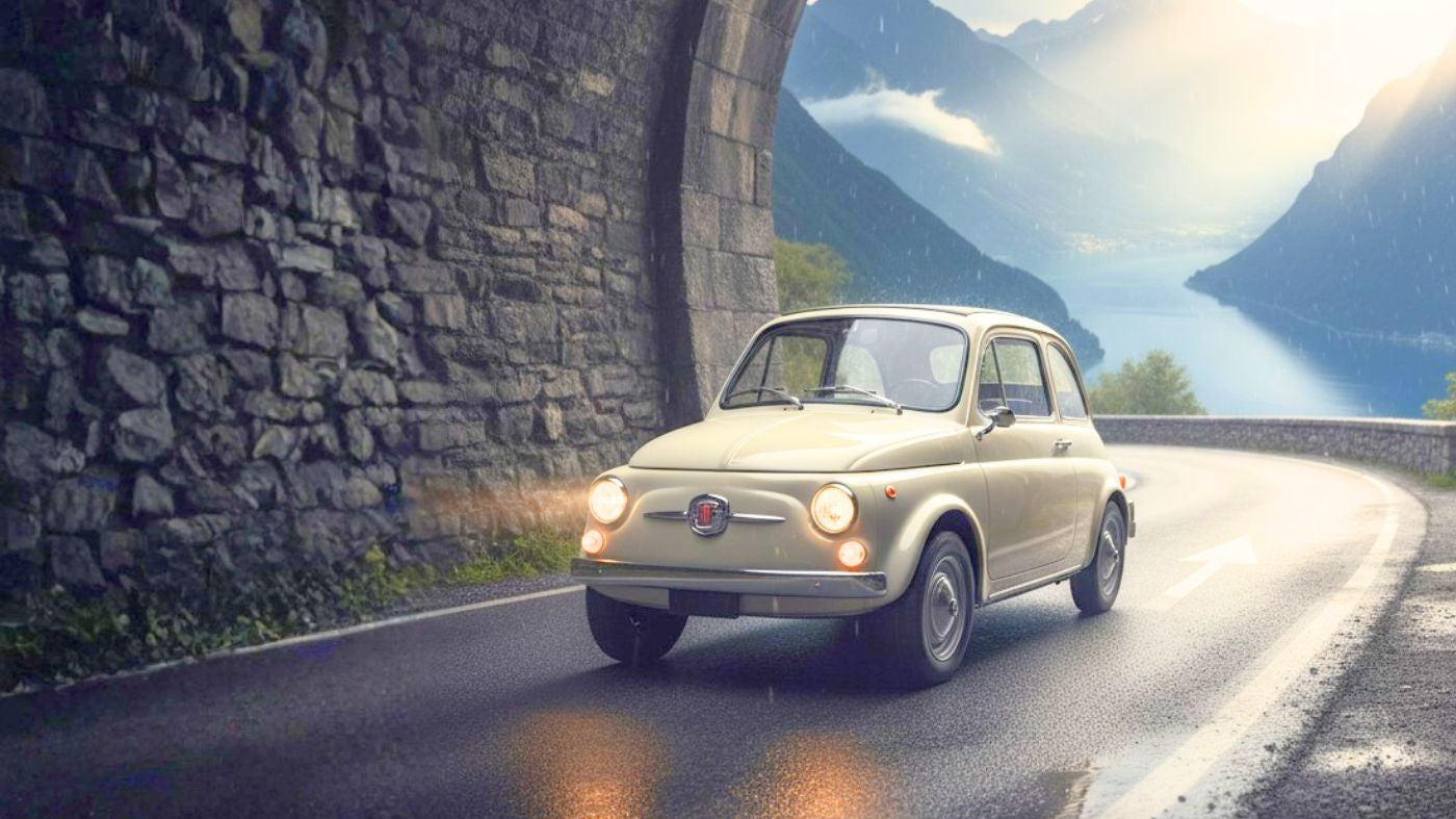 Fiat 500 d'epoca, colore carrozzeria avorio, entra in galleria su strada bagnata dalla pioggia in Italia. Illuminata da un raggio di sole. Fari accesi.